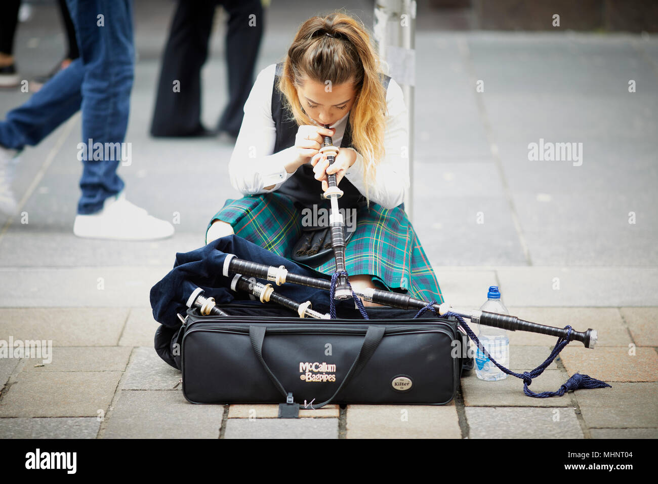 Glasgow in Scotland,  pretty  female lady bagpipe busker in traditional tartan suit   on Buchanan Street setting up Stock Photo