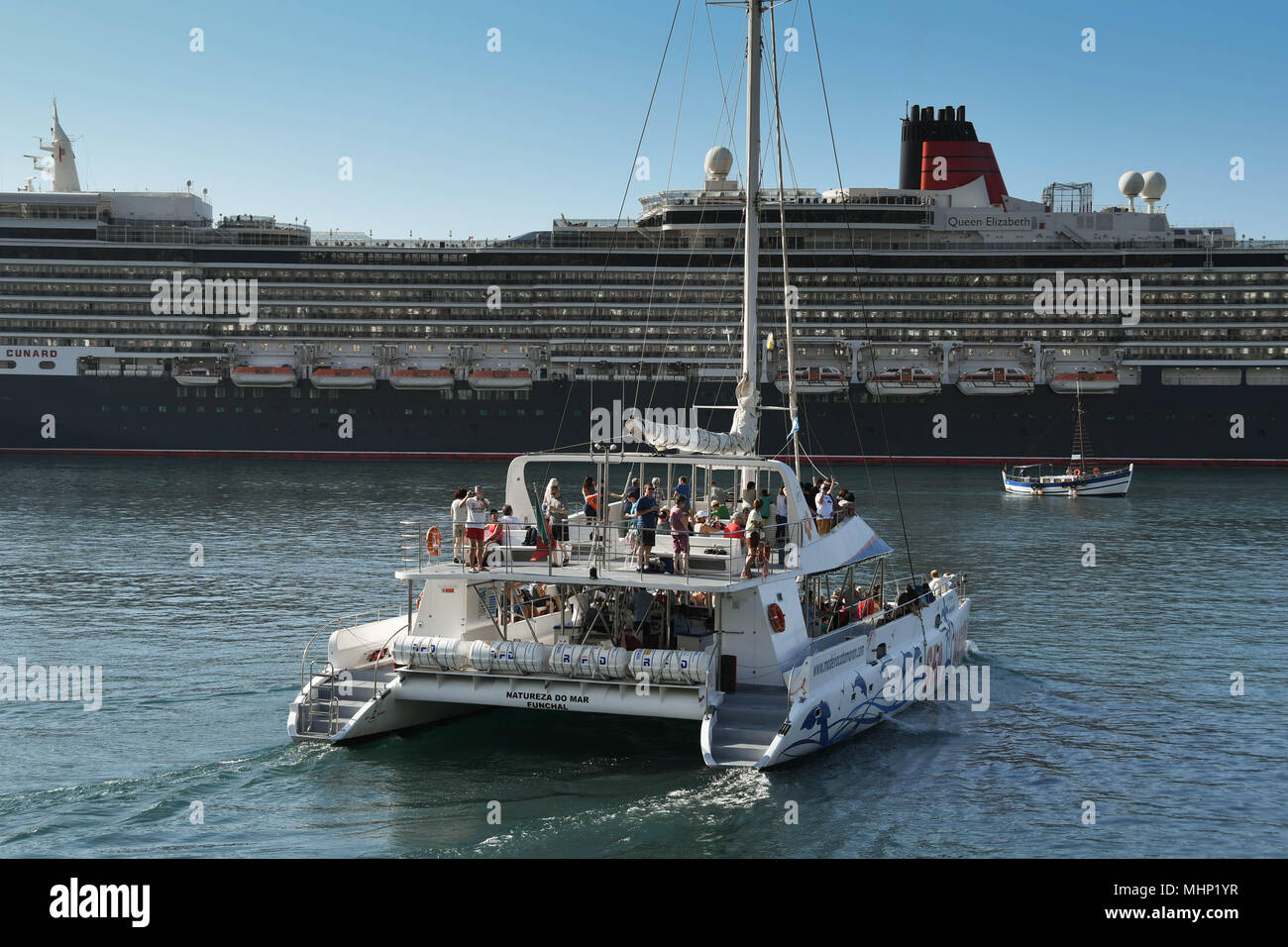 A catamaran leaving the harbour in Funchal, Madeira with tourists on a sightseeing cruise. The cruise liner Queen Elizabeth is in the background Stock Photo