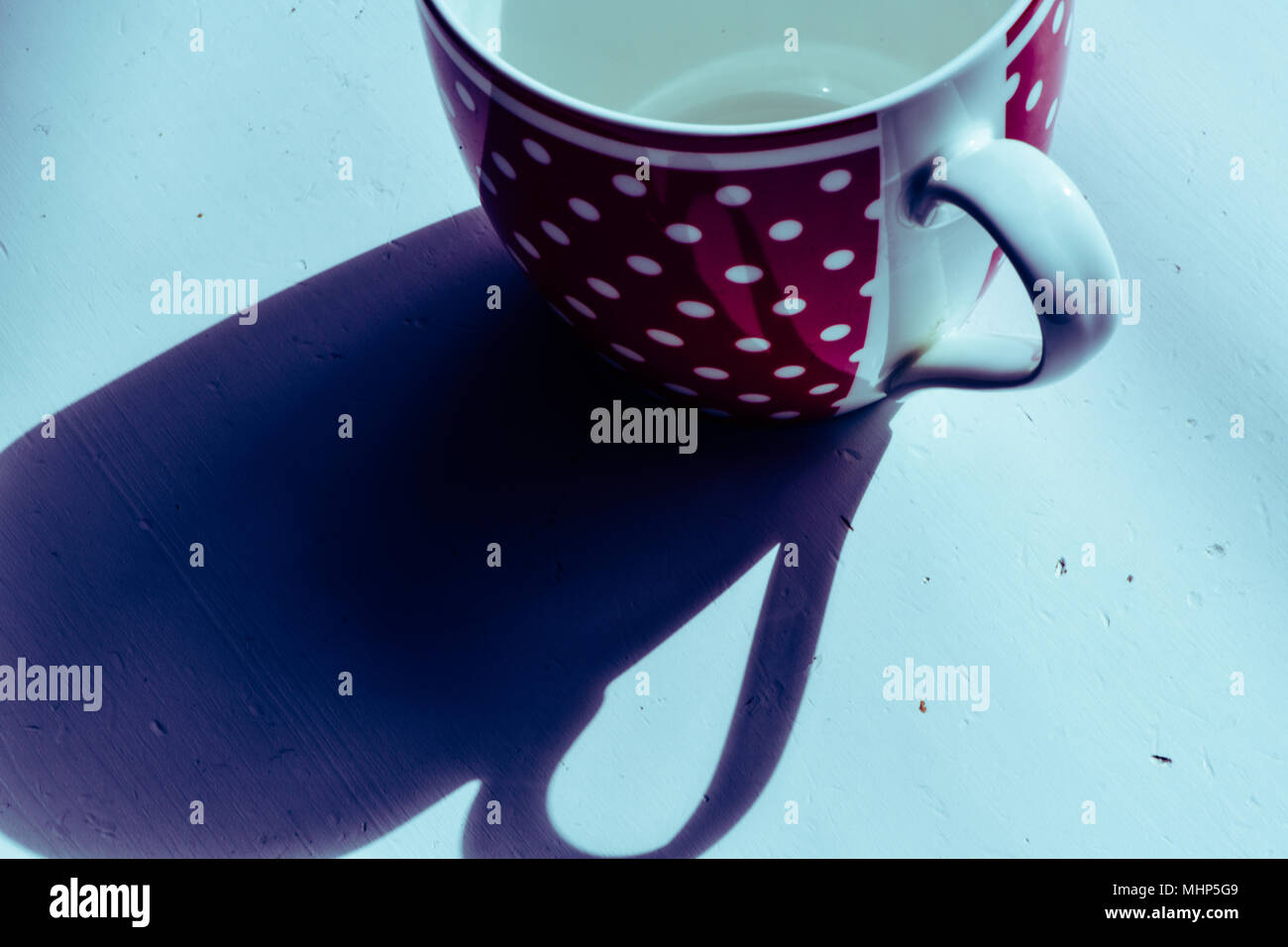 Red coffee mug with white spotted pattern on white table. Above with long shadows Stock Photo