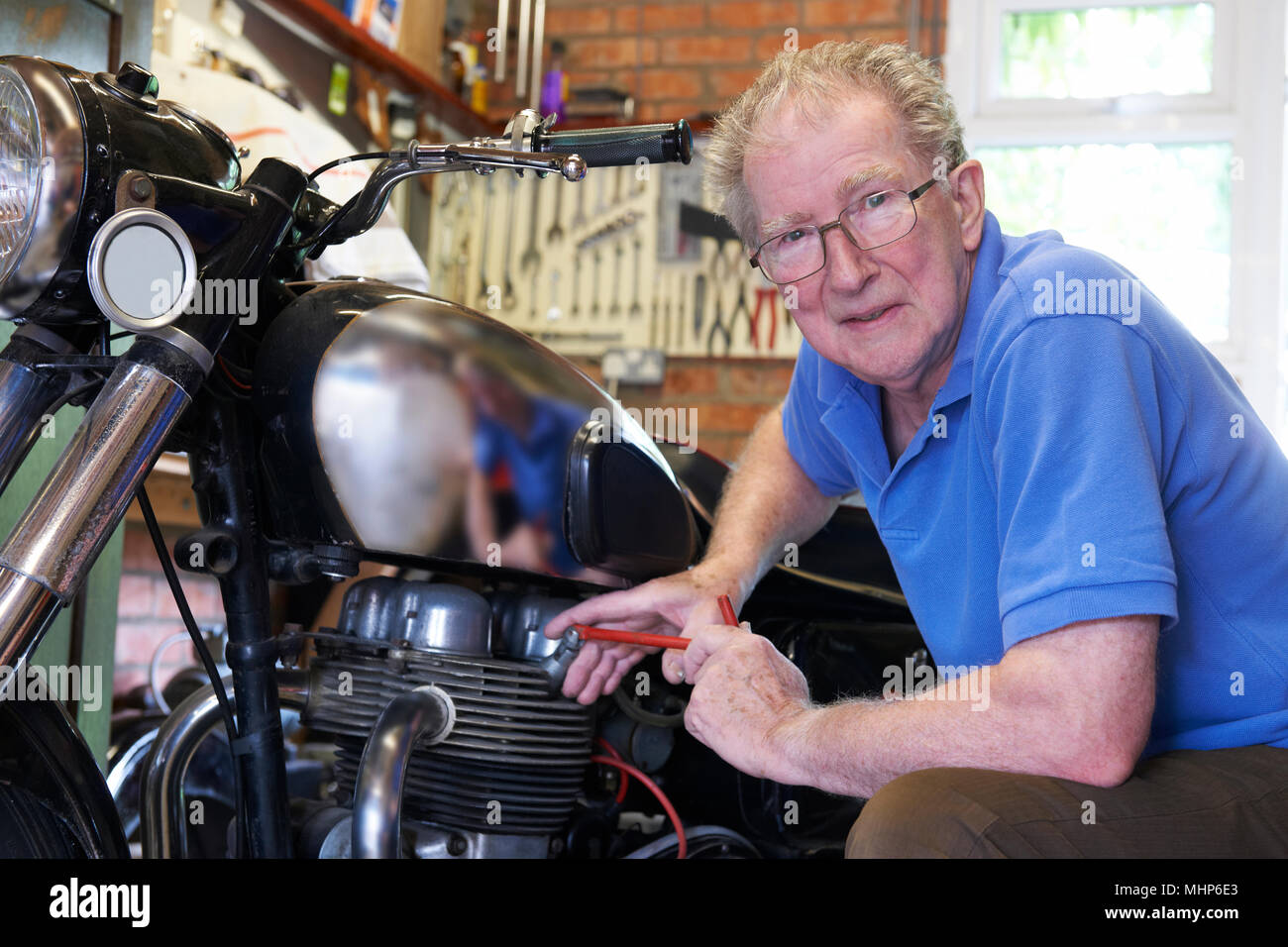 Portrait Of Senior Man Working On Vintage Motorcycle In Garage Stock Photo