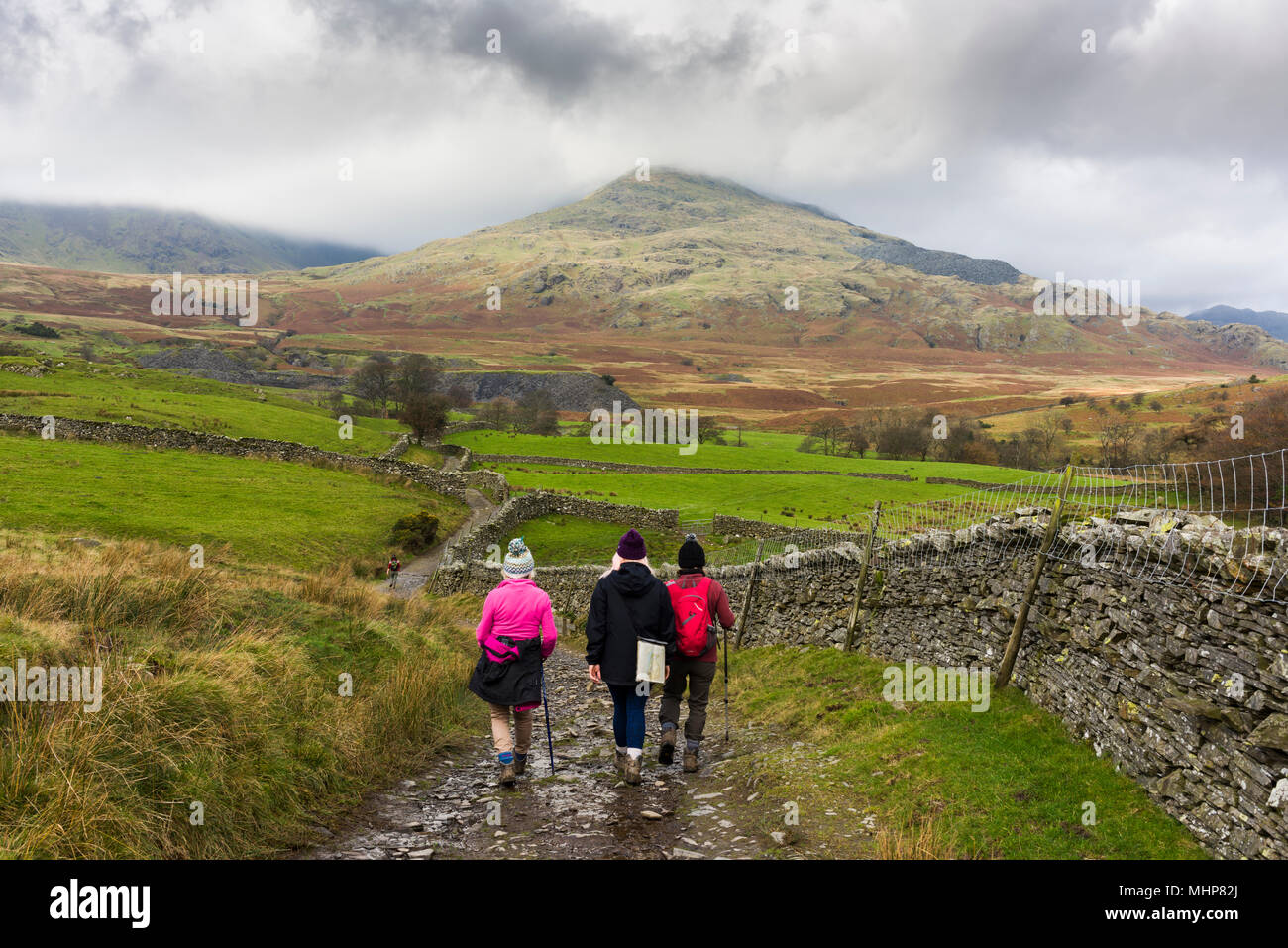 Walkers on an unmade lane near Torver with The Old Man of Coniston beyond in the Lake District National Park, Cumbria, England. Stock Photo