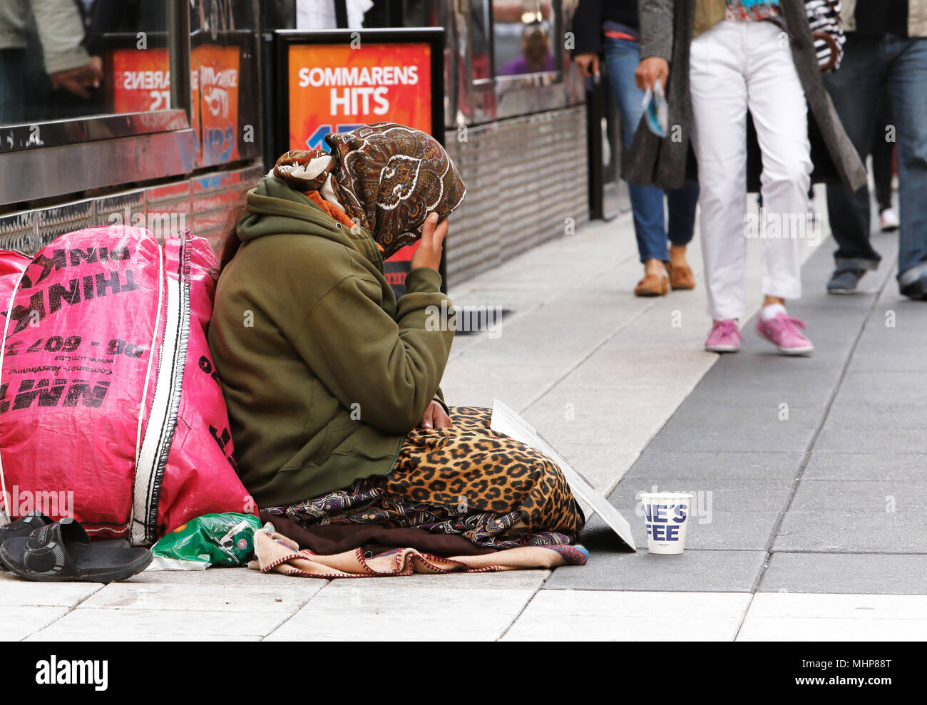 Stockholm, Sweden - June 24, 2014: An unknown woman sits quietly and asking for money with a mug in front of her on Drottninggatan. Stock Photo