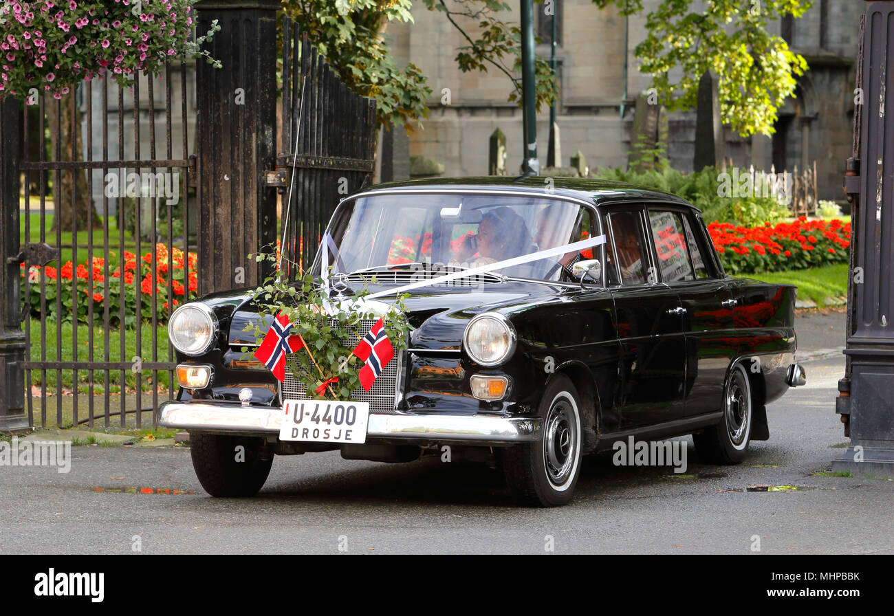 Trondheim, Norway - August 31, 2013: A newly married couple leave the cathedral in an older black Mercedes which is adorned with two Norwegian flags. Stock Photo