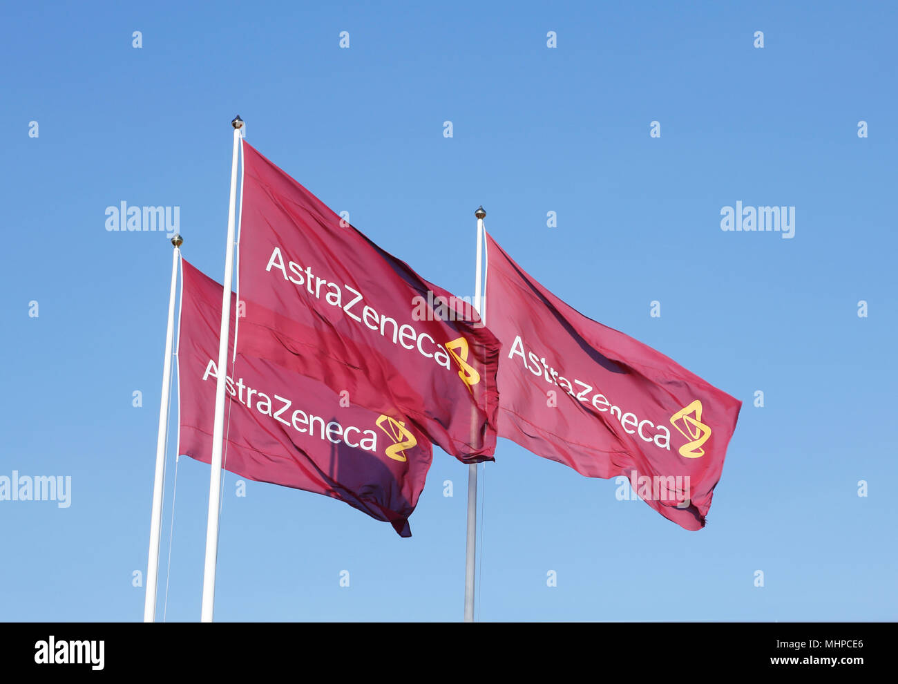 Sodertalje, Sweden - April 27, 2014: Three purple flags with the logo for Atrazeneca flying in the wind on top of the flagpoles against the blue sky. Stock Photo