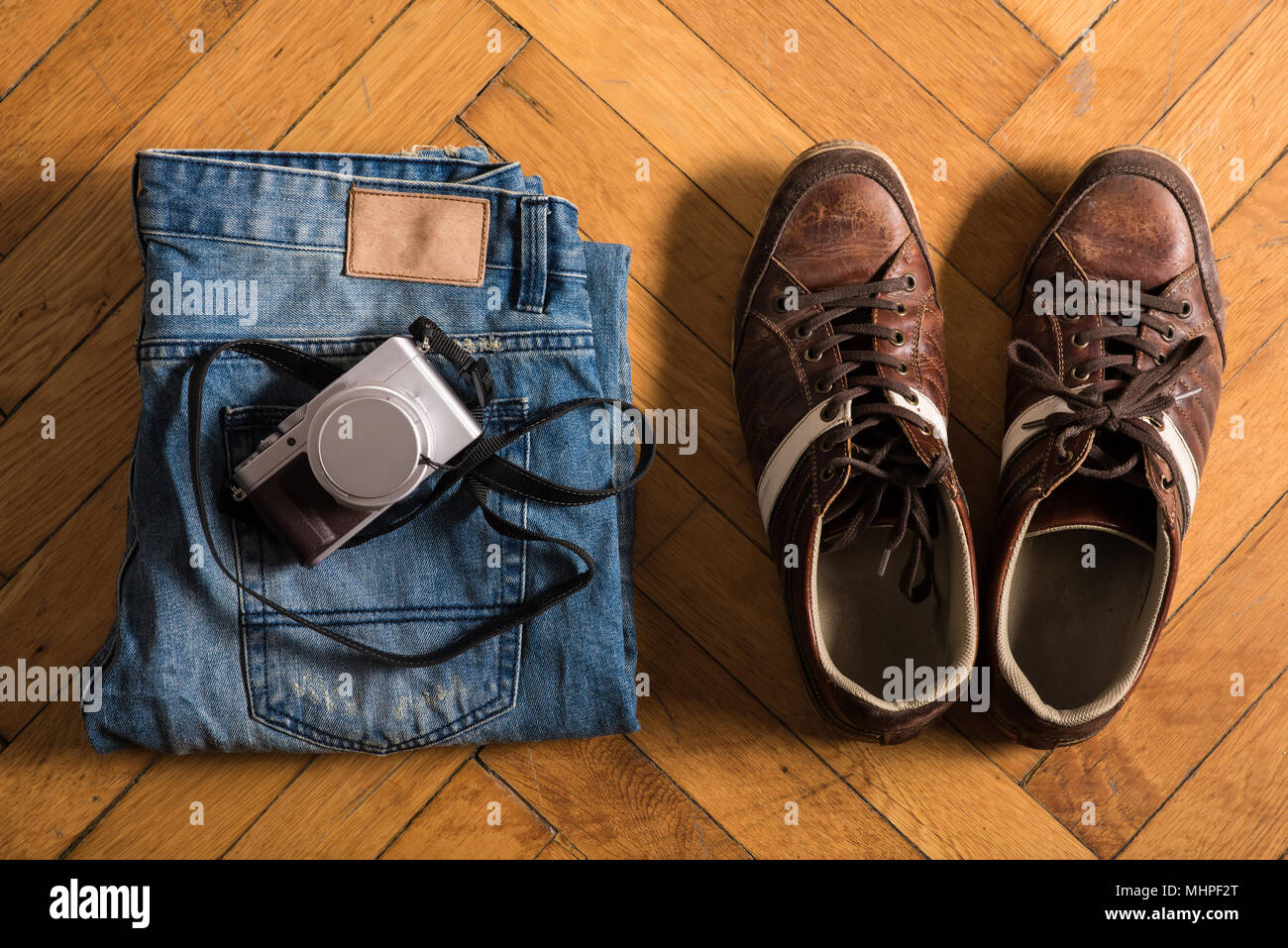 A pair of fretted blue jeans, brown shoes, and a camera lie by on the floor Stock Photo Alamy