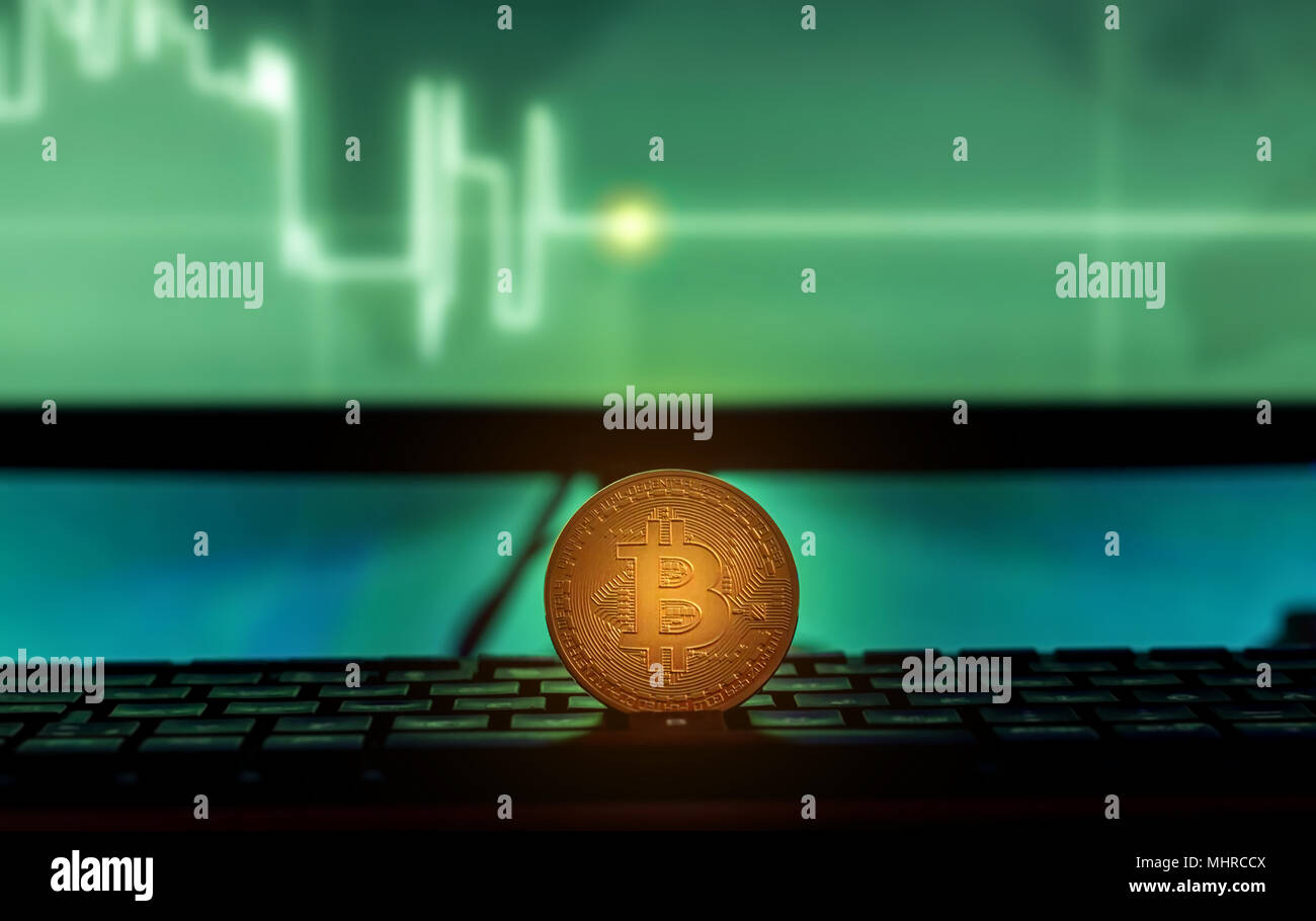 Physical Bitcoin placed on Laptop computer with charts on screen, dark ...