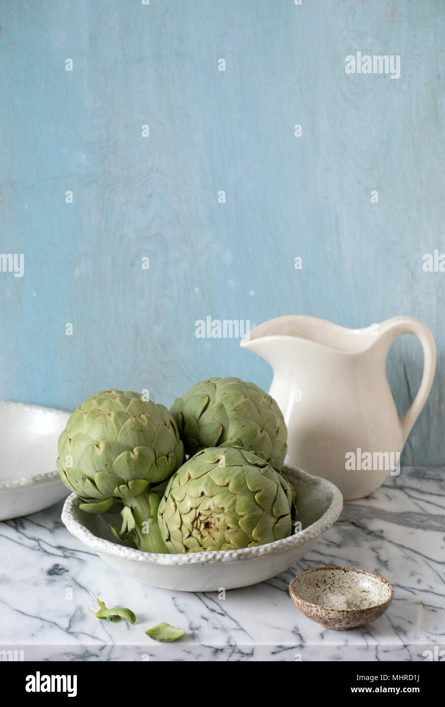 three artichokes ready in a white ceramic bowl with pitcher. Stock Photo