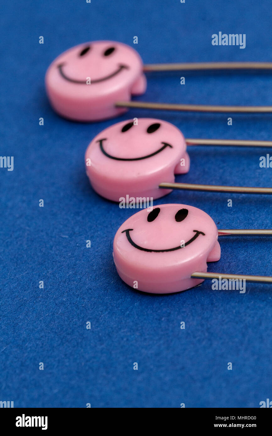 Plastic head metal safety pins pinned in paper. Pink smile emoticon