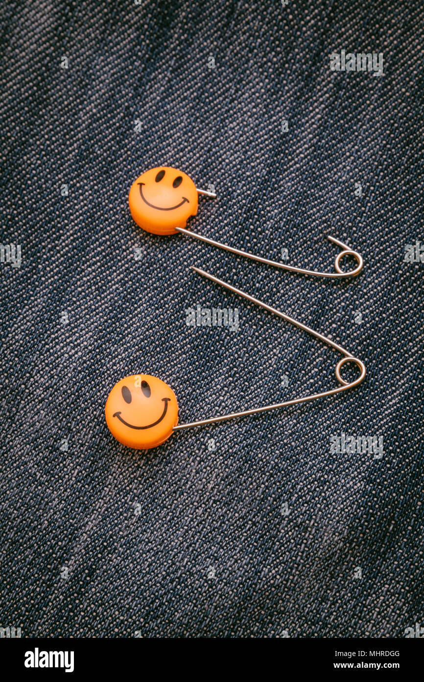 Plastic head metal safety pins pinned in jeans material. Orange smile emoticon safety pin. Cute and funny colorful emoticons. Stock Photo