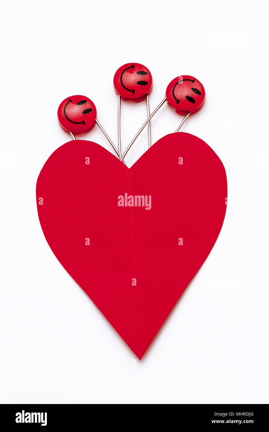 Plastic head metal safety pins pinned in heart shaped paper. Red smile