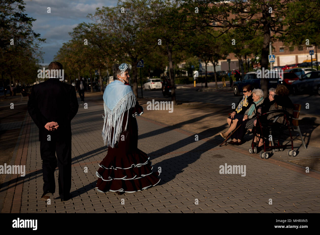 A woman wearing typical flamenco dress seen walking with her husband. “El día de la Cruz” or