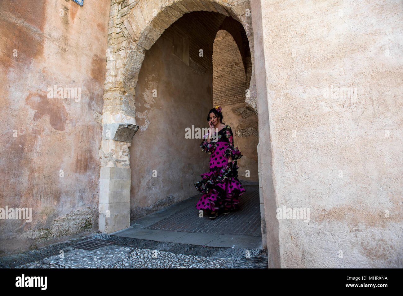 A girl wearing typical flamenco dress walking throught the gate of Arco de las Pesas. “El día de