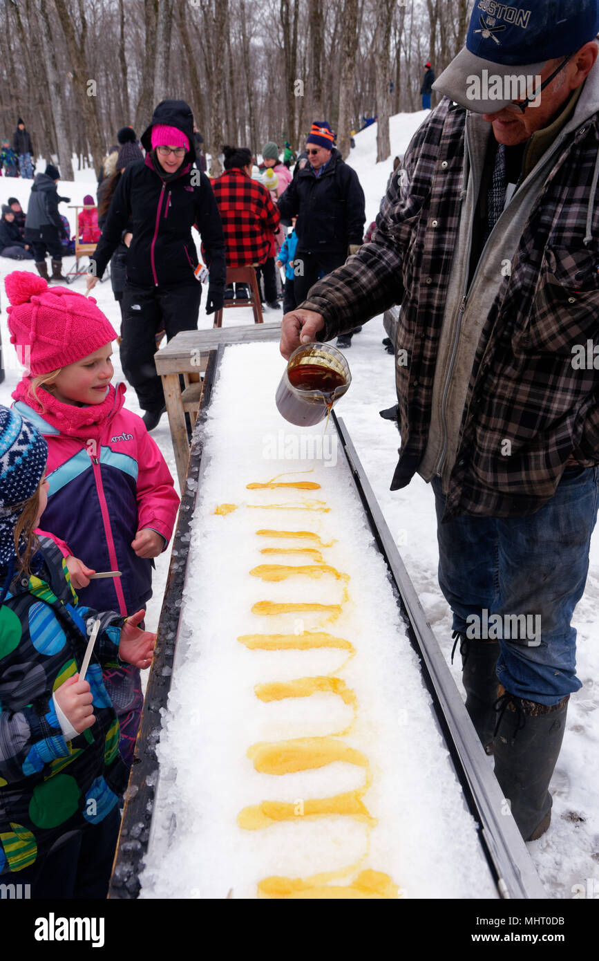 Children eating maple syrup taffy poured on ice at a sugar shack in Quebec, Canada Stock Photo