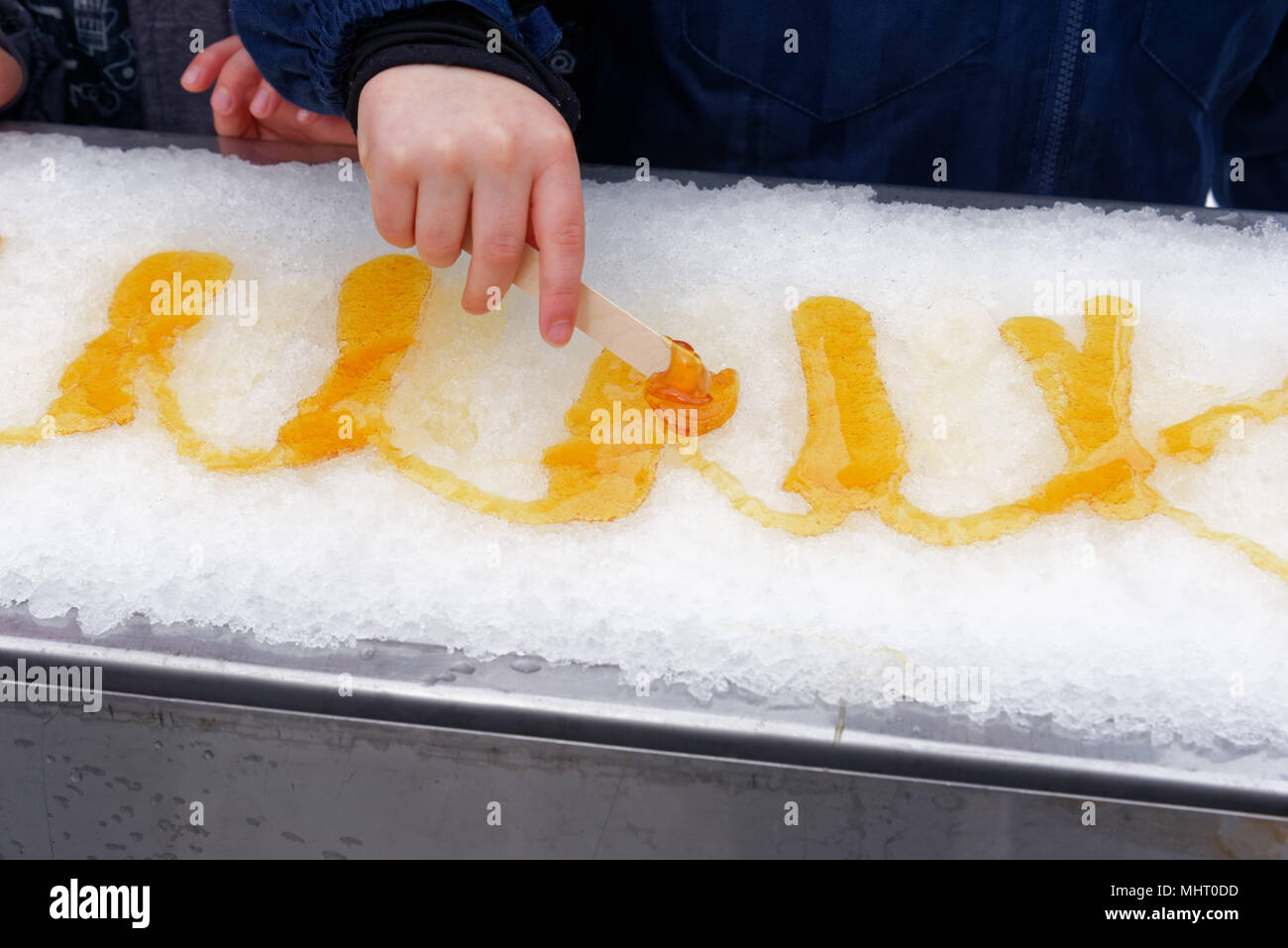 Close up of a young (5 yr old) child's hand rolling maple syrup taffy onto a stick Stock Photo