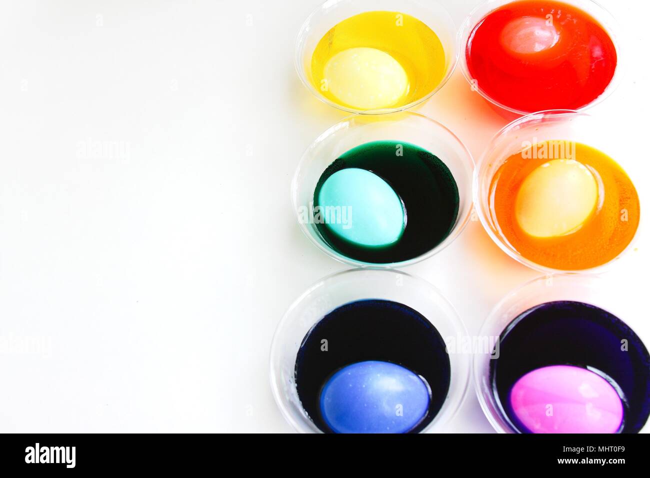 A bright and colorful image of eggs being dyed for Easter. Colored dyes in clear cups with egg in each one, different colors, isolated on white. Stock Photo