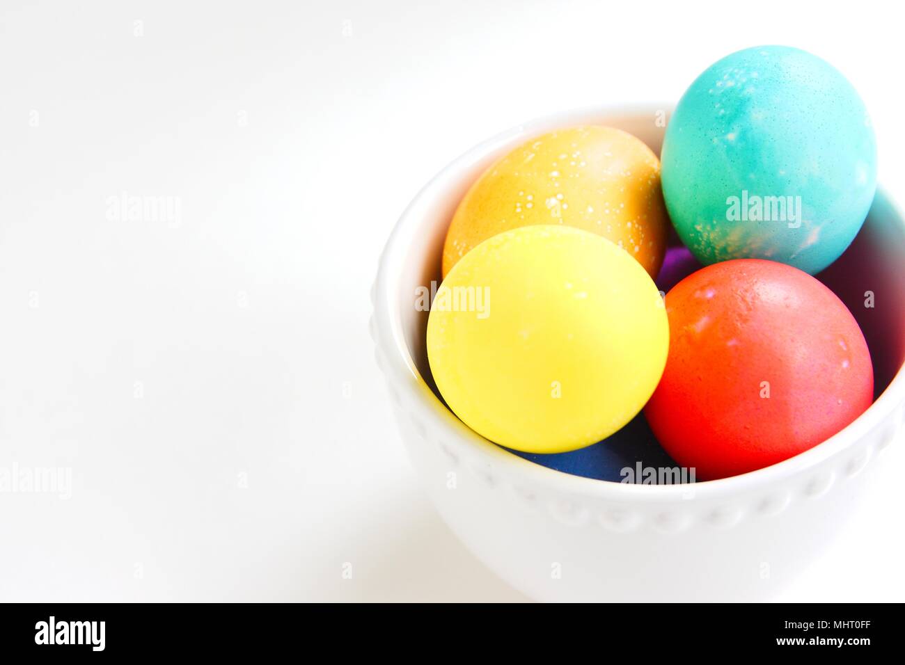 Brightly colored eggs in a white bowl on a white background Stock Photo