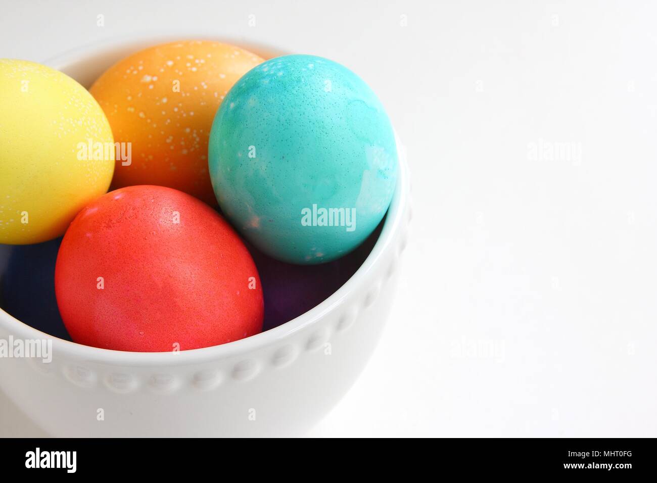 Brightly colored eggs in a white bowl on a white background Stock Photo