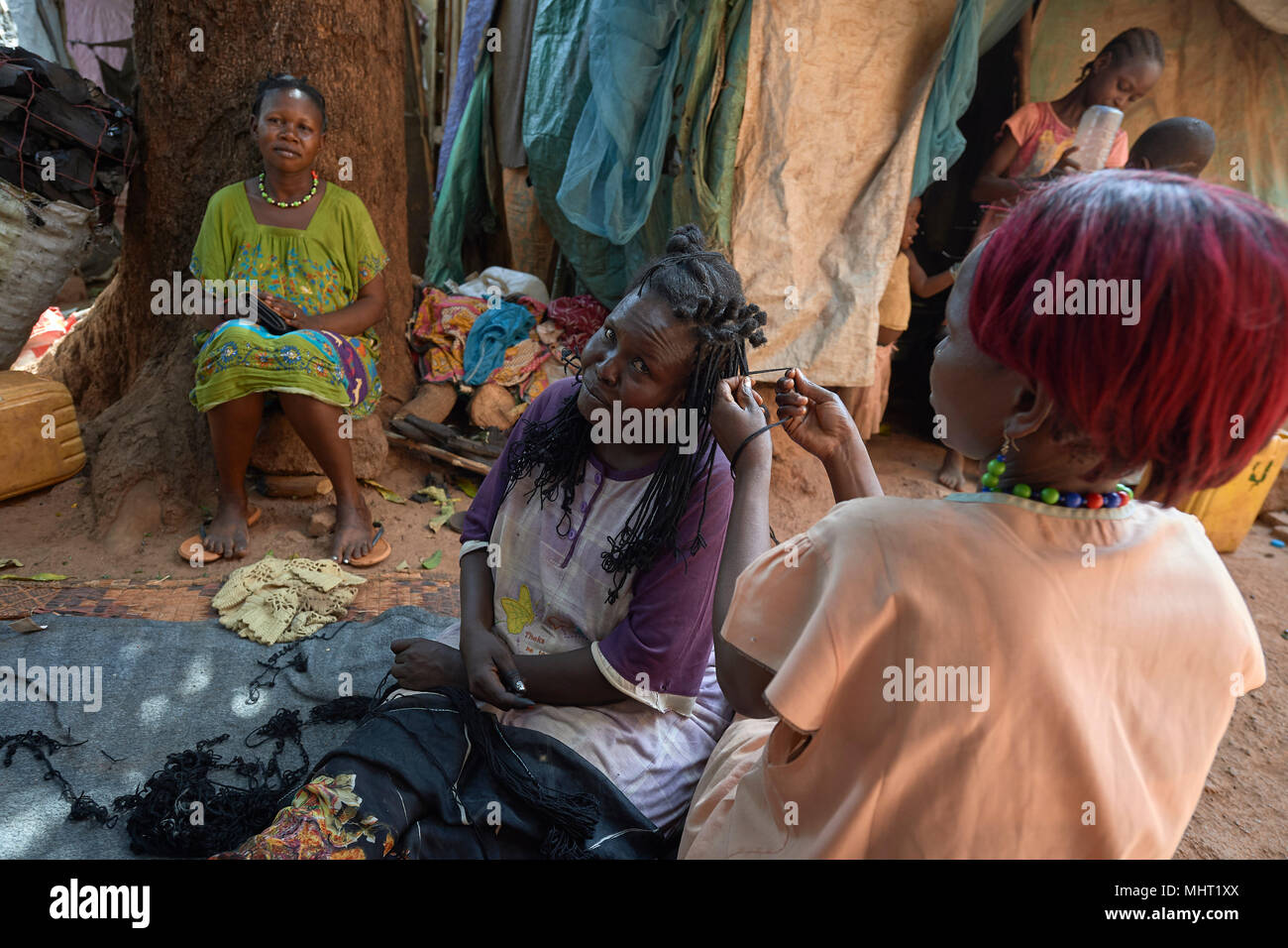 Margaret Ali braids the hair of Elizabeth Kwin in a camp for displaced families around the Catholic Cathedral of St. Mary in Wau, South Sudan. Stock Photo