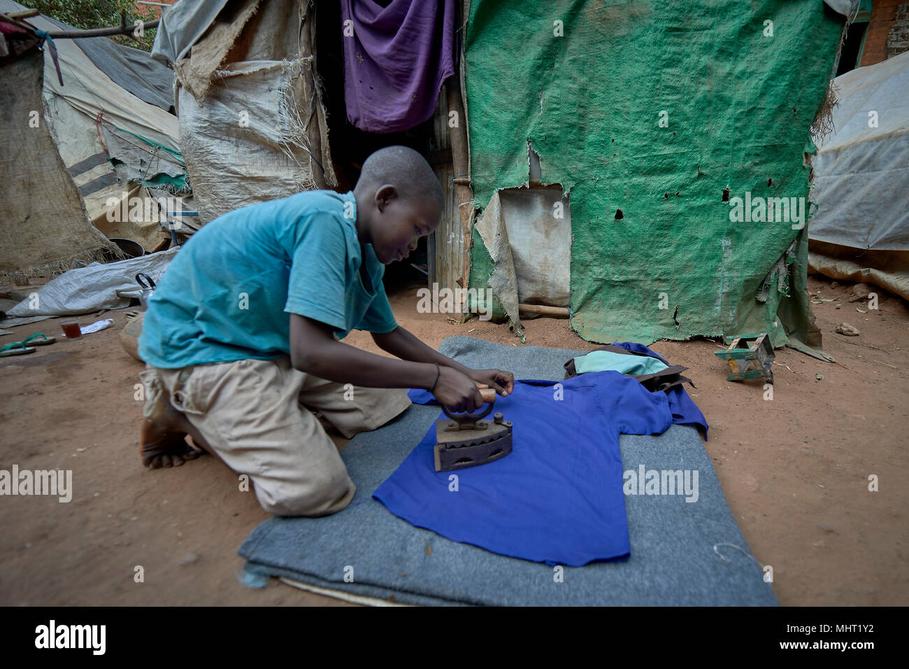 Johana Romano, an 11-year old boy displaced by war, irons his school uniform in a camp for displaced around the Catholic Cathedral in Wau, South Sudan. Stock Photo