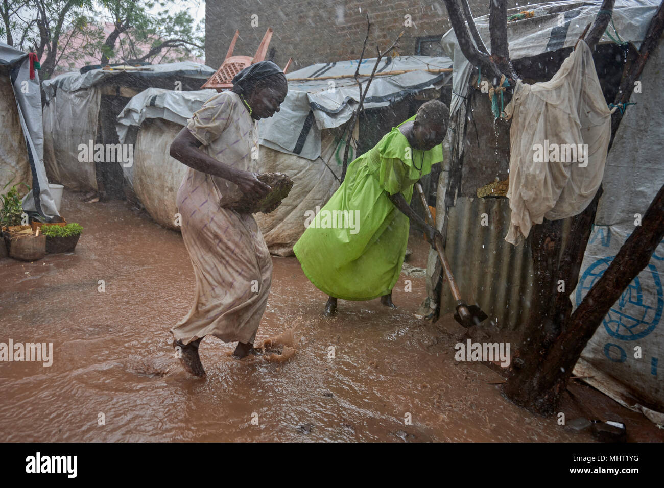 Rene Abdallah (left) and Anjima Fahal struggle to keep water out of their shelter during a rainstorm in a displaced persons camp in Wau, South Sudan. Stock Photo