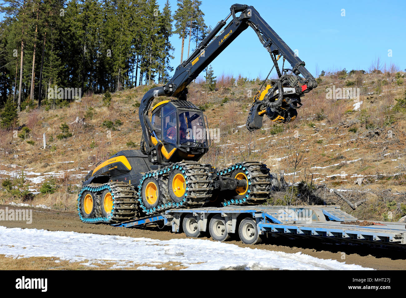 Forest machine operator drives Ponsse Scorpion King harvester onto transport trailer on a sunny day of spring in Salo, Finland - March 31, 2018. Stock Photo