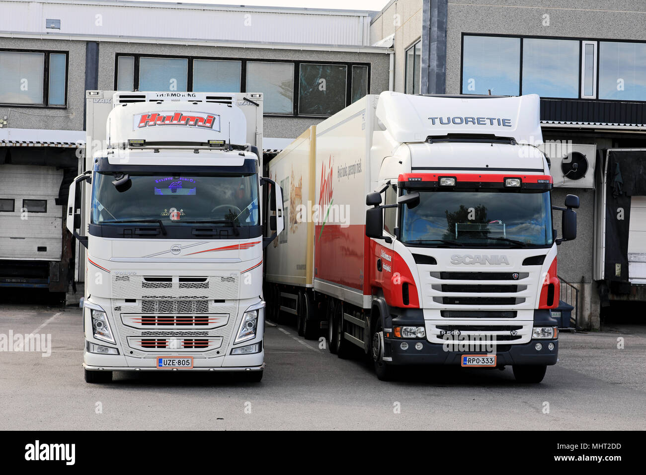 Two red and white refrigerated trailer trucks unloading at warehause loading zone on a clear summer afternoon in Salo, Finland - July 21, 2017. Stock Photo