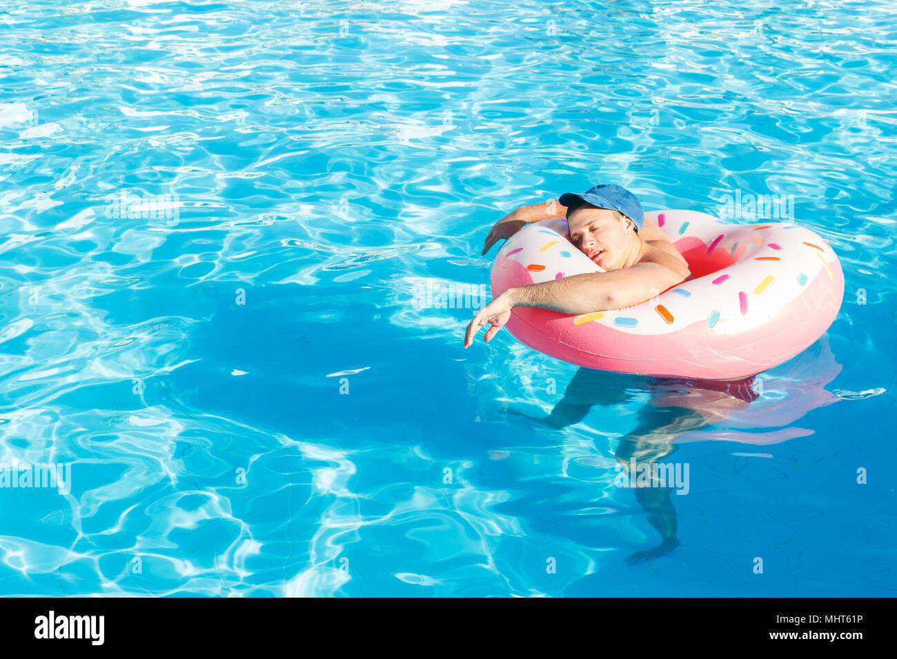 top view of young drunk guy swim with pink circle in pool. drunk guy on vacation in the hotel