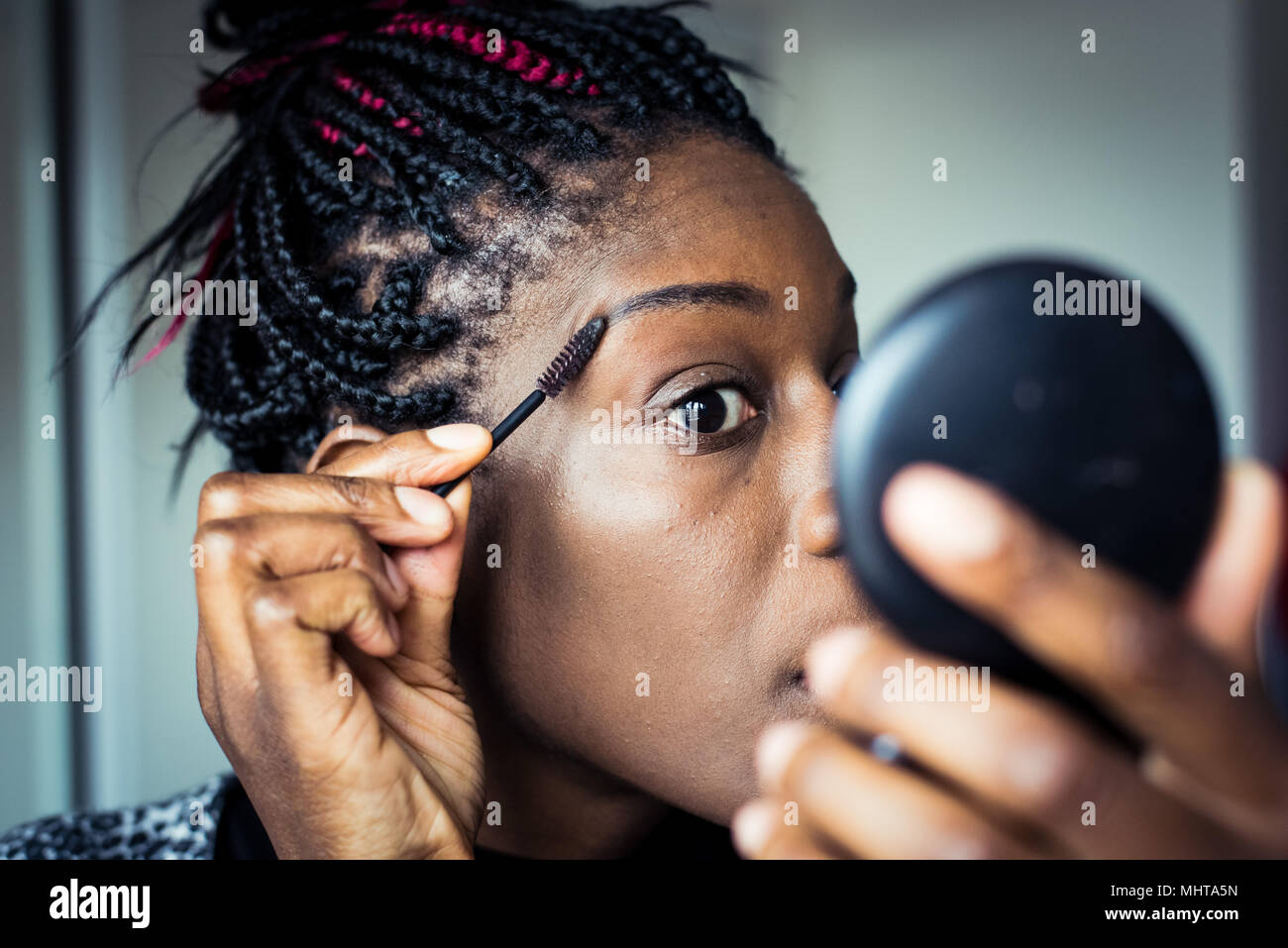 Black woman preparing for a night out, applying makeup in a hand mirror Stock Photo