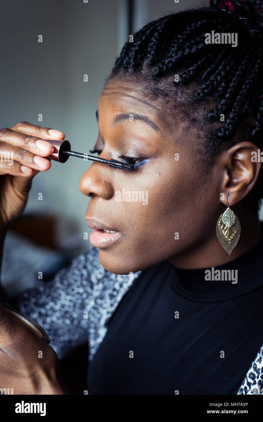 Black woman preparing for a night out, applying makeup in a hand mirror Stock Photo