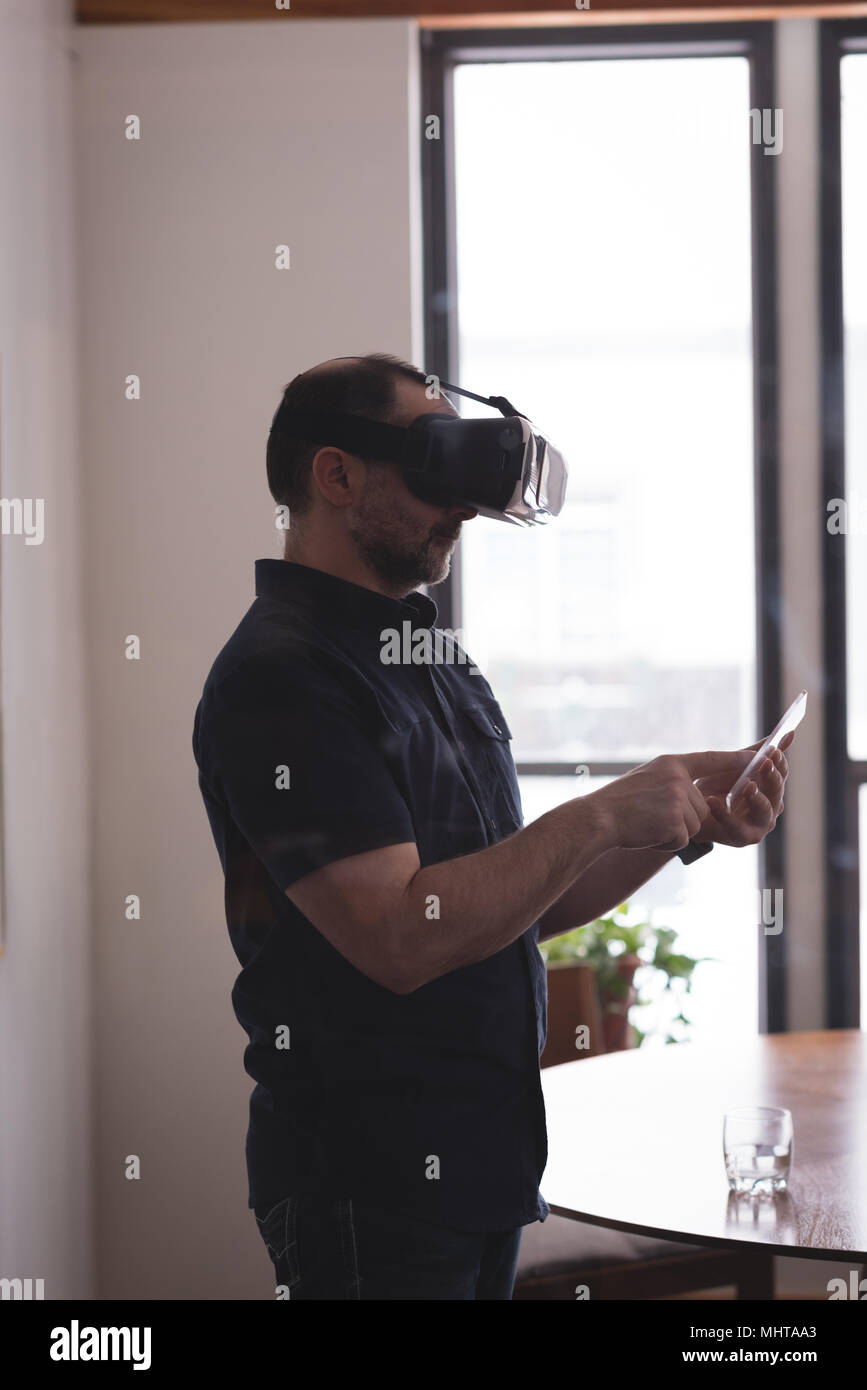 Male executive using virtual reality headset with glass digital tablet Stock Photo