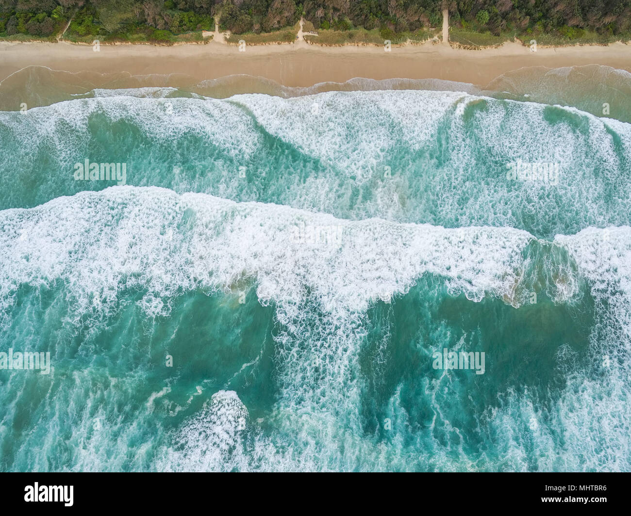 Looking down at large ocean waves breaking on sandy beach Stock Photo