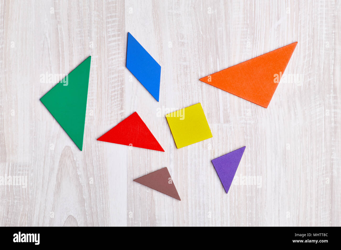 Colored geometric pieces of puzzle like triangles, square and parallelogram, are scattered on a light wooden background Stock Photo