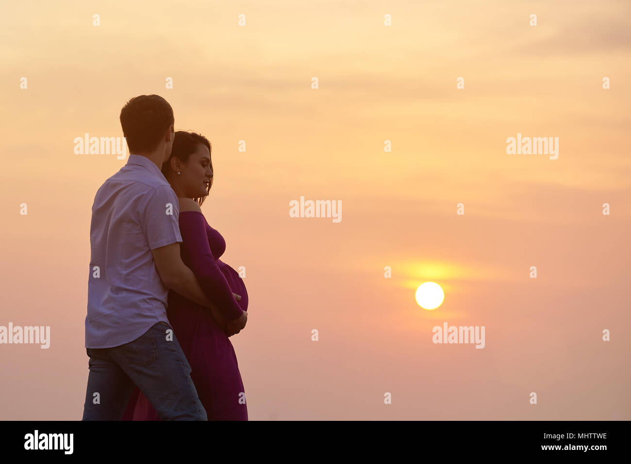 Silhouette of man hugging pregnant woman on sunset background Stock Photo