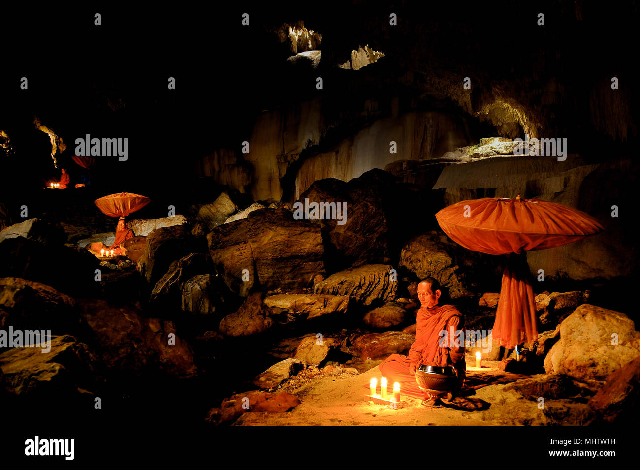 Kanchanaburi, Thailand - July 15, 2011: Buddhist monks sitting with alms bowl, lighten candle and long-handles umbrella to do individual meditation in Stock Photo