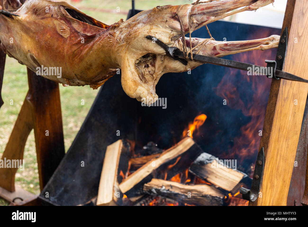 Lamb body spit-roasts over the open fire. Golden brown meat, drops of hot fat. Burning firewood and clouds of smoke. Preparation of food in a medieval Stock Photo