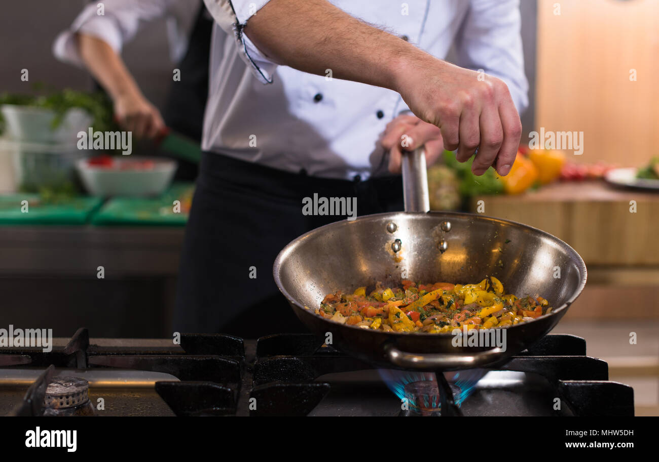 Young male chef putting spices on vegetables in wok at commercial ...