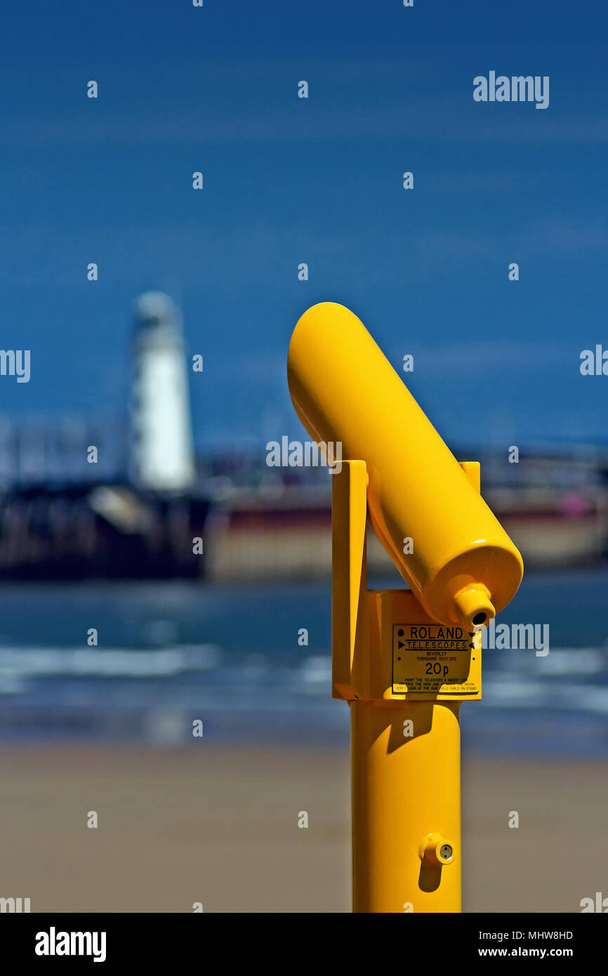 A brilliant yellow viewing telescope in Scarborough’s South Bay, against a background of the town’s harbour and lighthouse. Stock Photo