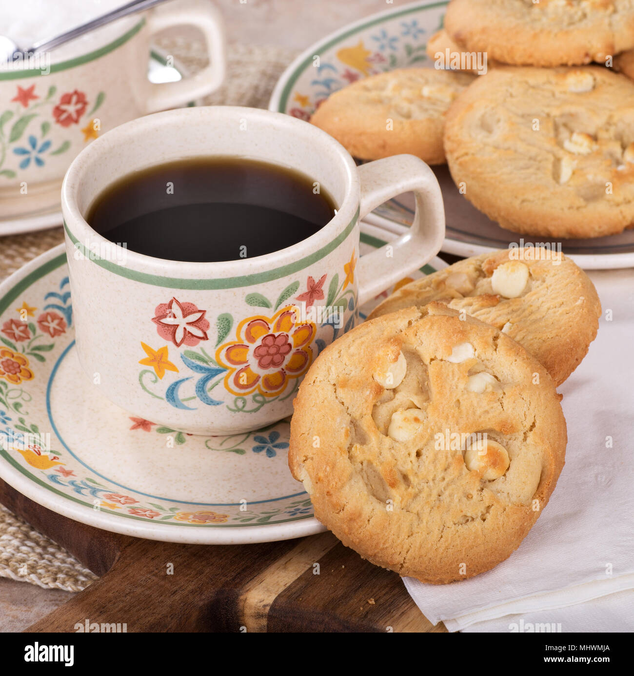 White chocolate macadamia cookies and cup of coffee on a plate with a plate of cookies and bowl of sugar in background Stock Photo