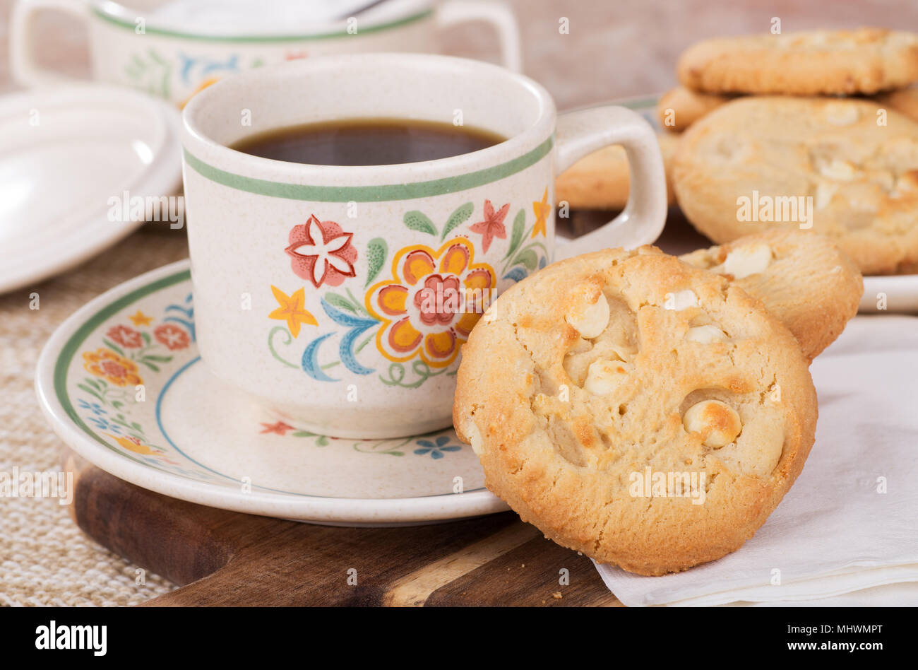 White chocolate macadamia cookies and cup of coffee on a plate with a plate of cookies and bowl of sugar in background Stock Photo