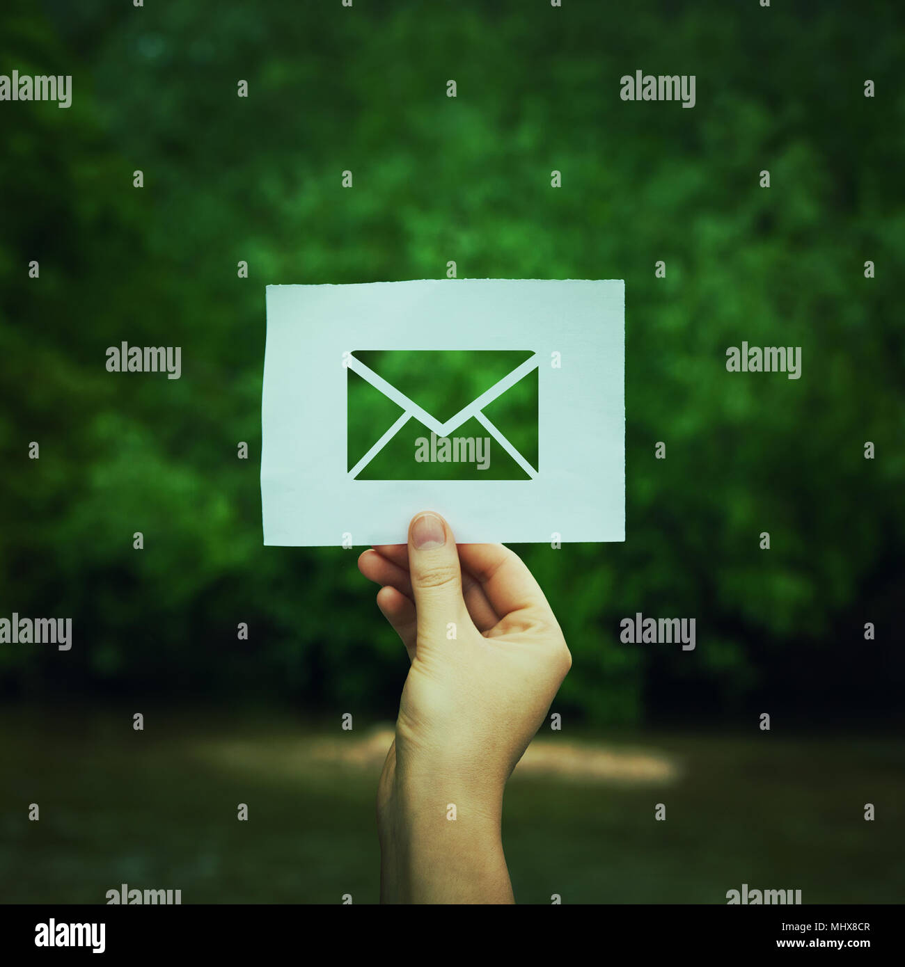 Woman hand holding a paper sheet with envelope message icon over green forest nature background. Ecology and greening concept, global environmental is Stock Photo