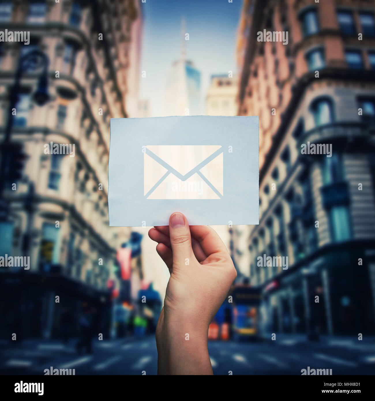 Woman hand holding a paper sheet with envelope message icon over city street background. Big city life new email incoming message. Bussiness social ne Stock Photo