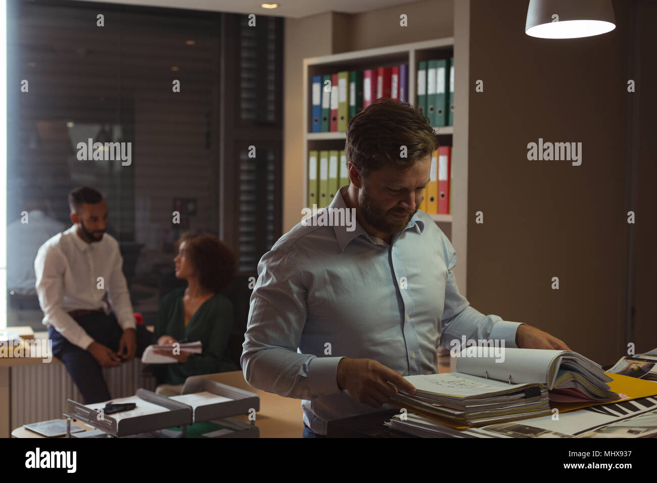 Architect checking file while colleagues interacting in background