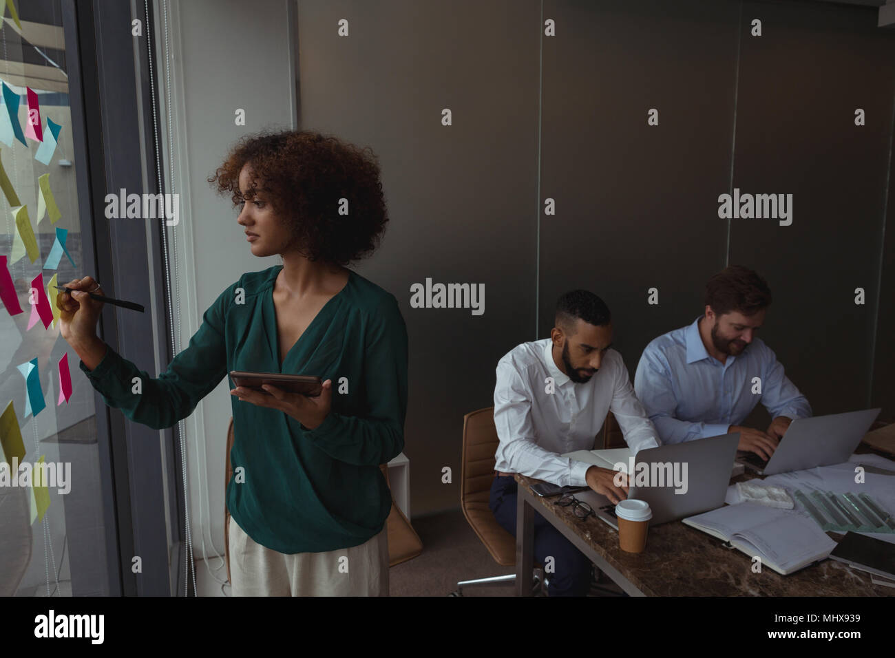 Female Architect with digital tablet writing on sticky note while colleagues using laptop Stock Photo
