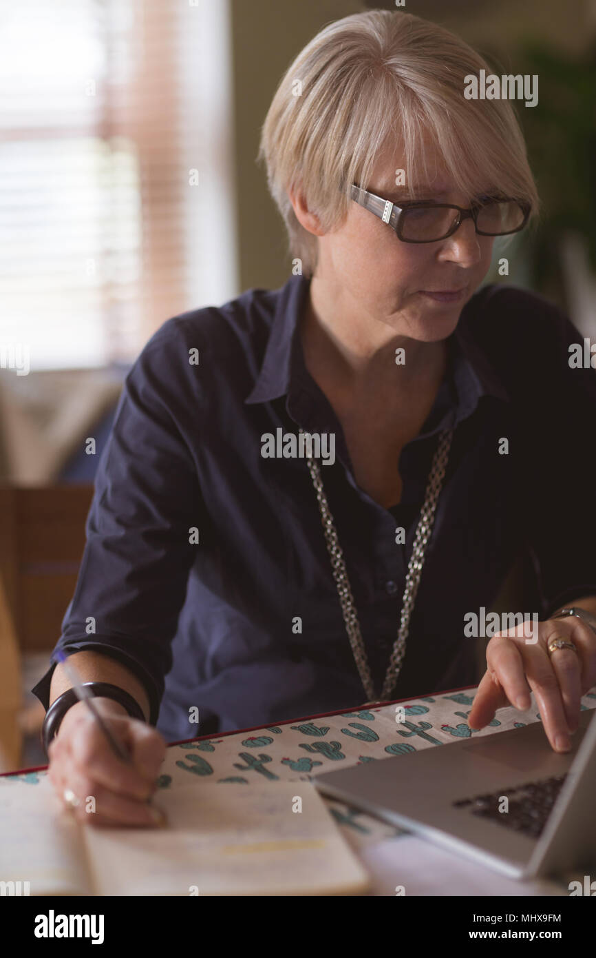 Mature woman using laptop while writing in diary Stock Photo