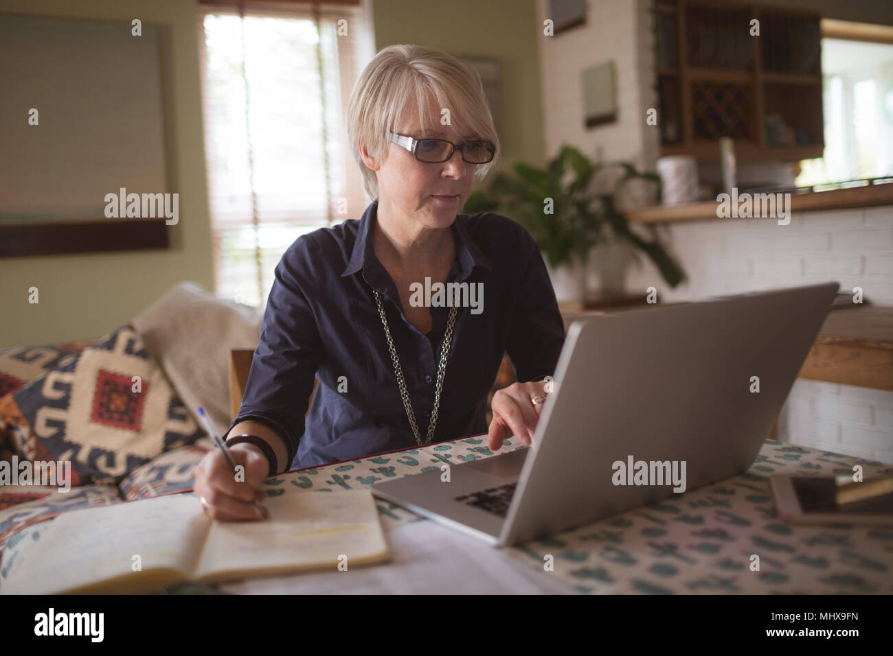 Mature woman using laptop while writing in diary Stock Photo