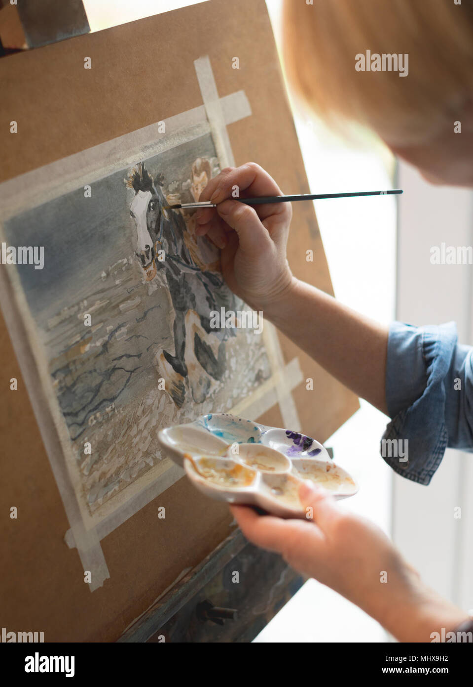 Female artist painting on a canvas with a paintbrush and holding a color palette Stock Photo