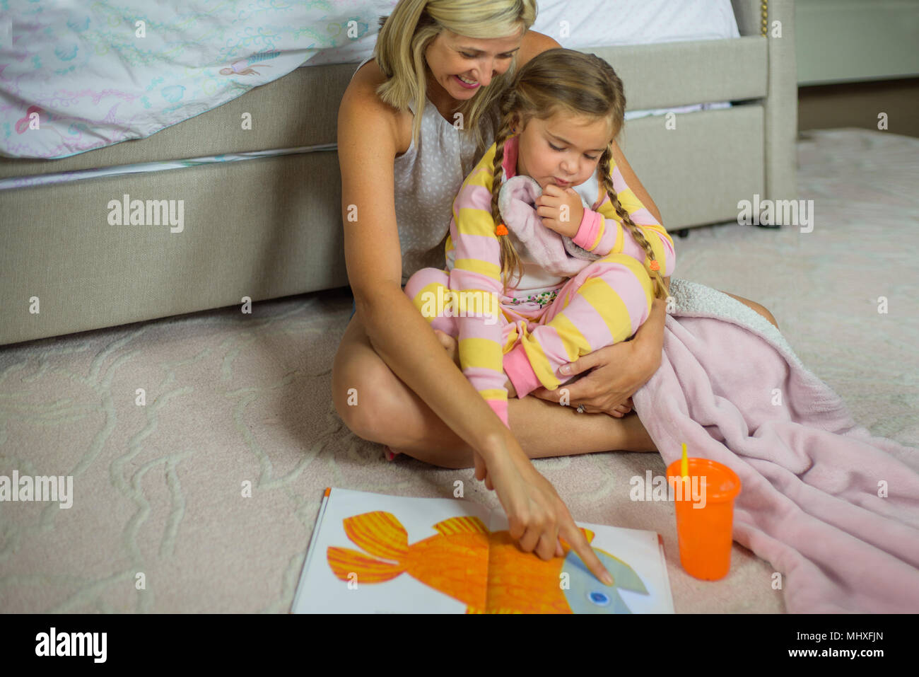 Mid adult woman sitting on floor with daughter at bedtime looking at picture book Stock Photo