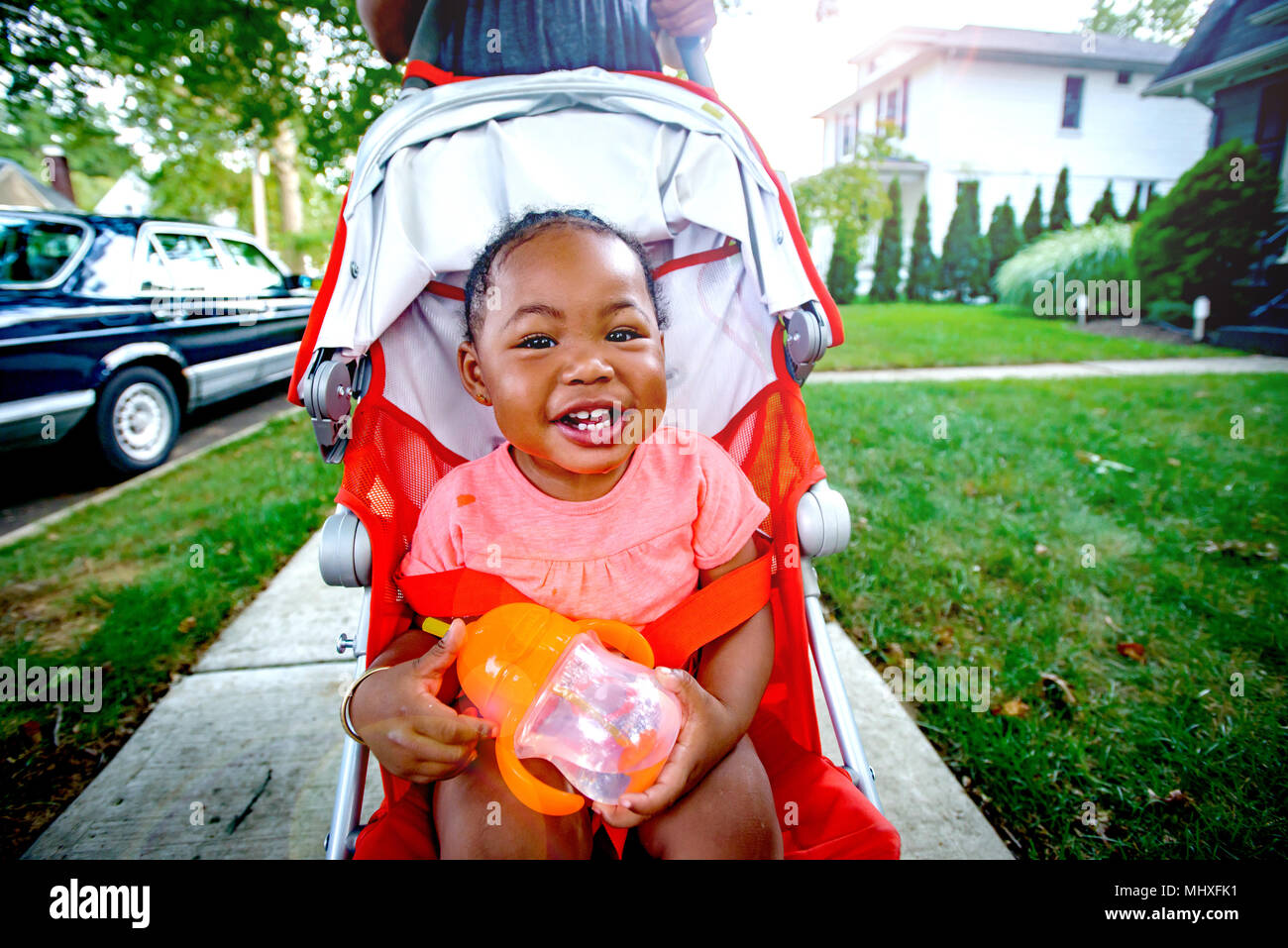 Happy baby girl in pushchair on suburban sidewalk, portrait Stock Photo