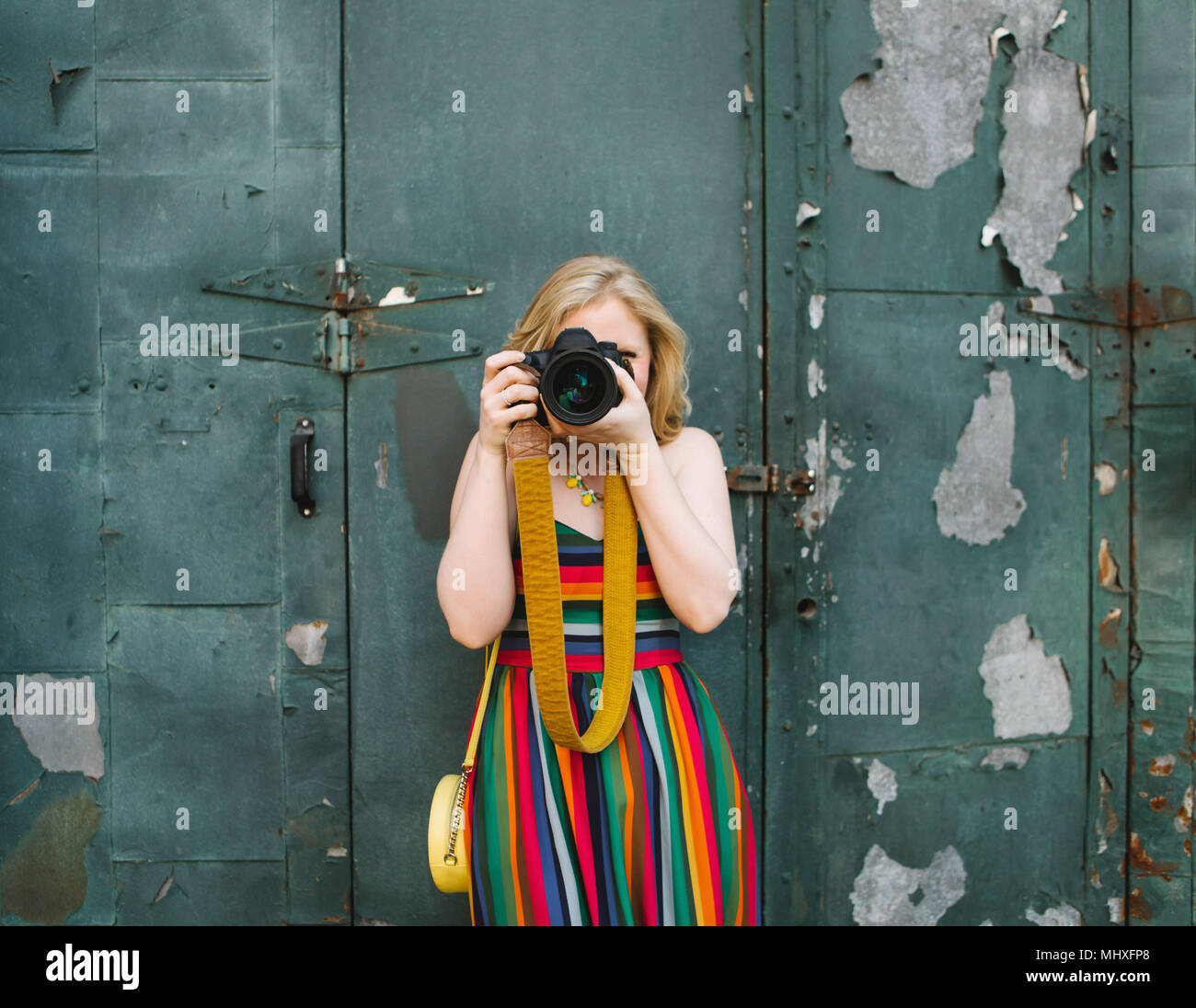 Young woman in striped dress in front of industrial door taking photographs, portrait Stock Photo