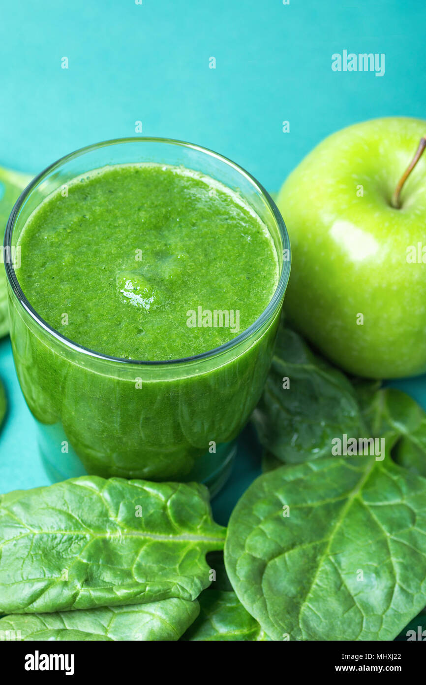 Glass with Green Fresh Smoothie from Leafy Greens Vegetables Fruits Bananas Kiwi Cucumber. Scattered Spinach Leaves Apple on Turquoise Background. Hea Stock Photo
